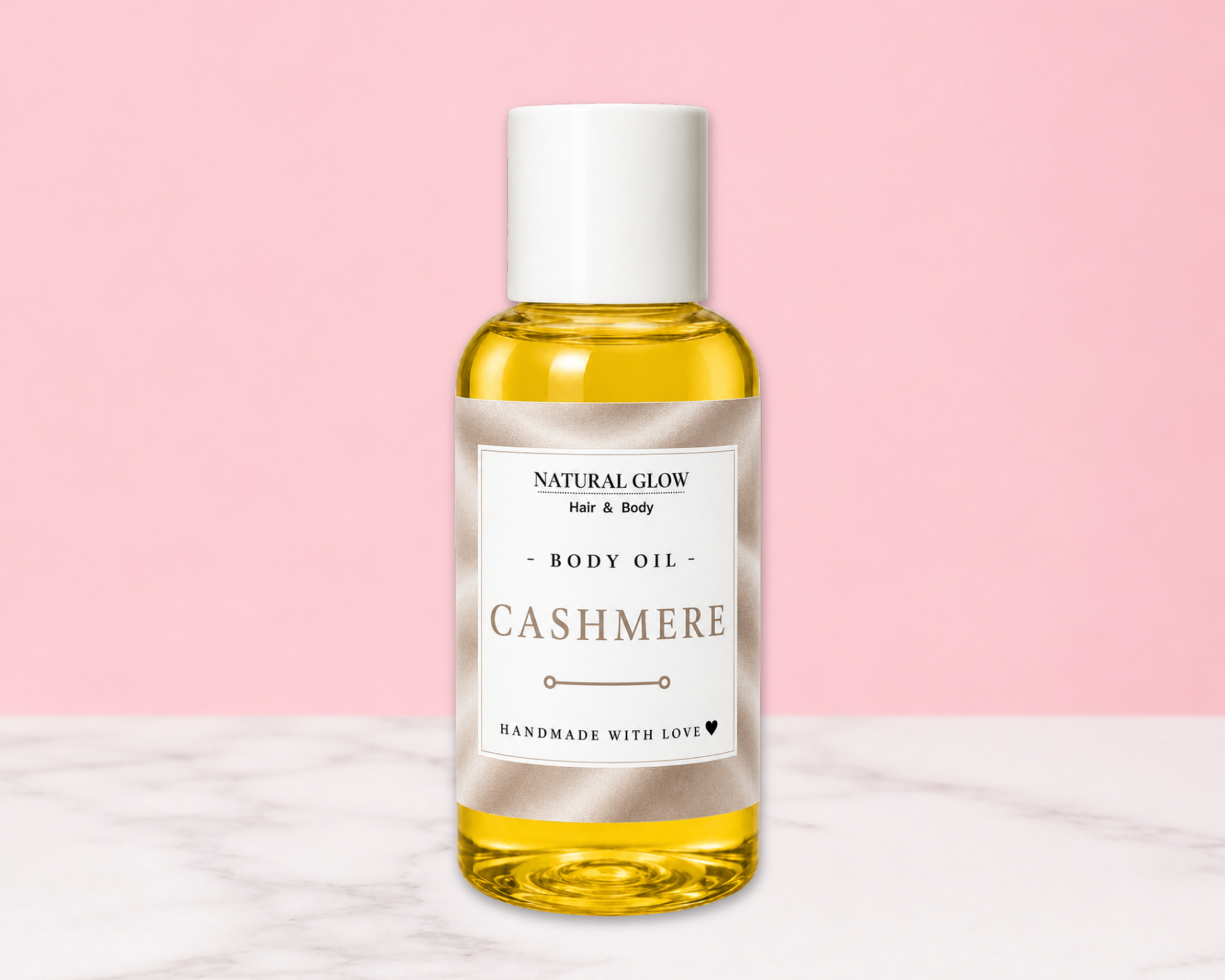 A bottle of Natural Glow Cashmere Hair & Body Oil, filled with golden yellow oil, featuring a white cap and a cream-colored label, set against a soft pink background with a white marble surface.