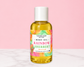 A bottle of Natural Glow Rainbow Sherbert body oil with a white cap and a colorful tropical label, set against a pink background with a white marble surface.