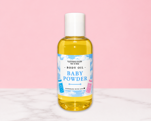 A bottle of Natural Glow For & Baby Baby Powder Body Oil, filled with yellow liquid and featuring a white cap, set against a pink background with a white marble surface.