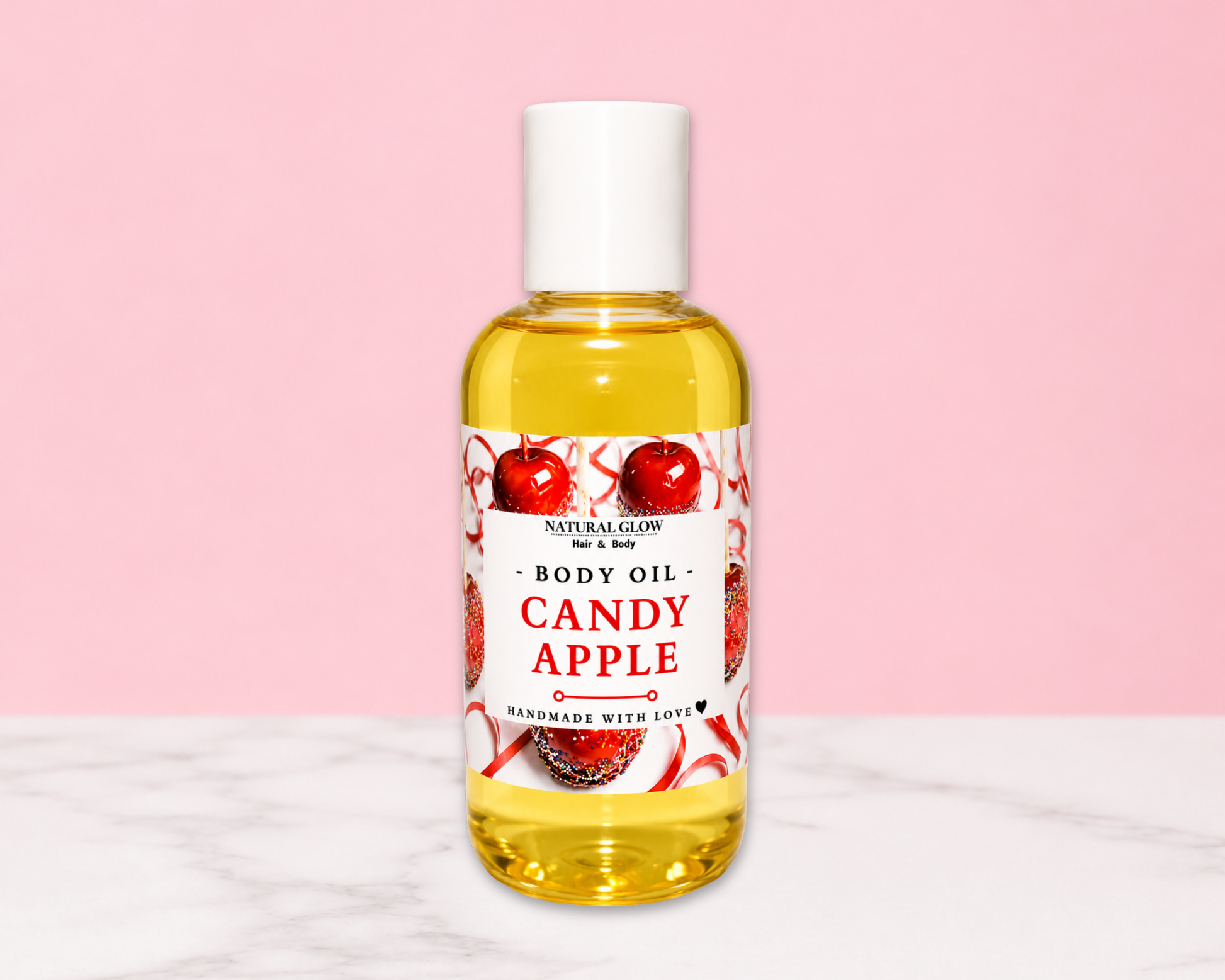 A bottle of Natural Goods Body Oil in the Candy Apple scent, filled with yellow oil and featuring a white cap, set against a pink background with a white marble surface.