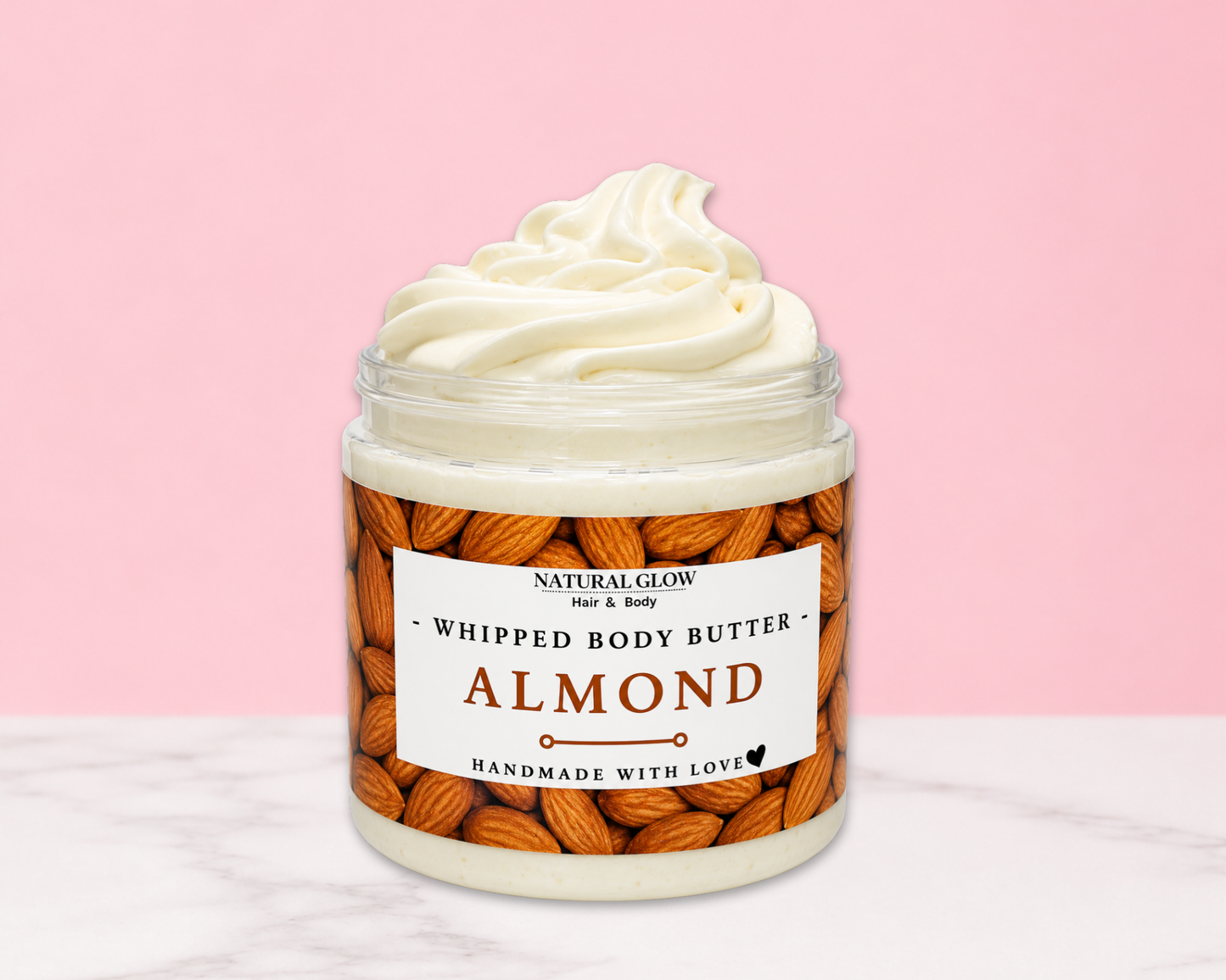 Natural Glow Almond whipped body butter in a jar with cream-colored butter swirl, pink background, and white marble surface