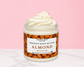 Natural Glow Almond whipped body butter in a jar with cream-colored butter swirl, pink background, and white marble surface