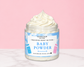 Natural Glow Baby Powder whipped body butter in a jar with cream-colored butter swirl, pink background, and white marble surface