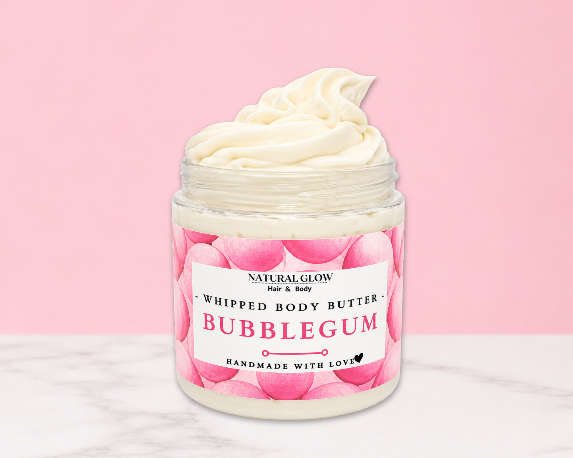 Natural Glow Bubblegum whipped body butter in a jar with cream-colored butter swirl, pink background, and white marble surface