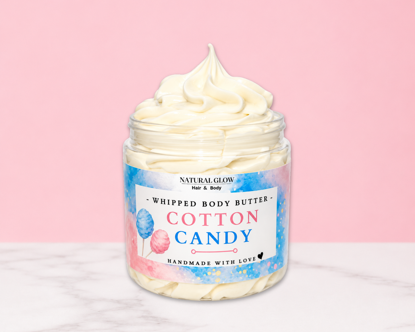 Natural Glow Cotton Candy whipped body butter in a jar with cream-colored butter swirl, pink background, and white marble surface