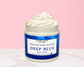 Natural Glow Deep Blue men's whipped body butter in a jar with cream-colored butter swirl, pink background, and white marble surface