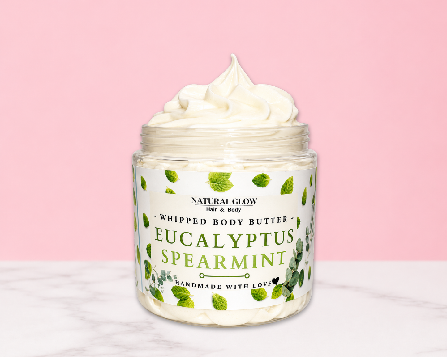 Natural Glow Eucalyptus & Spearmint whipped body butter in a jar with cream-colored butter swirl, pink background, and white marble surface