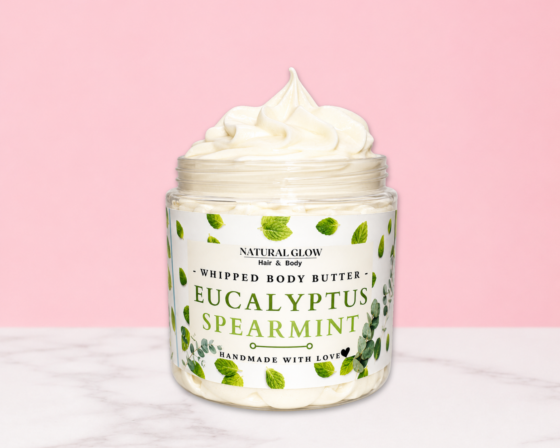 Natural Glow Eucalyptus & Spearmint whipped body butter in a jar with cream-colored butter swirl, pink background, and white marble surface