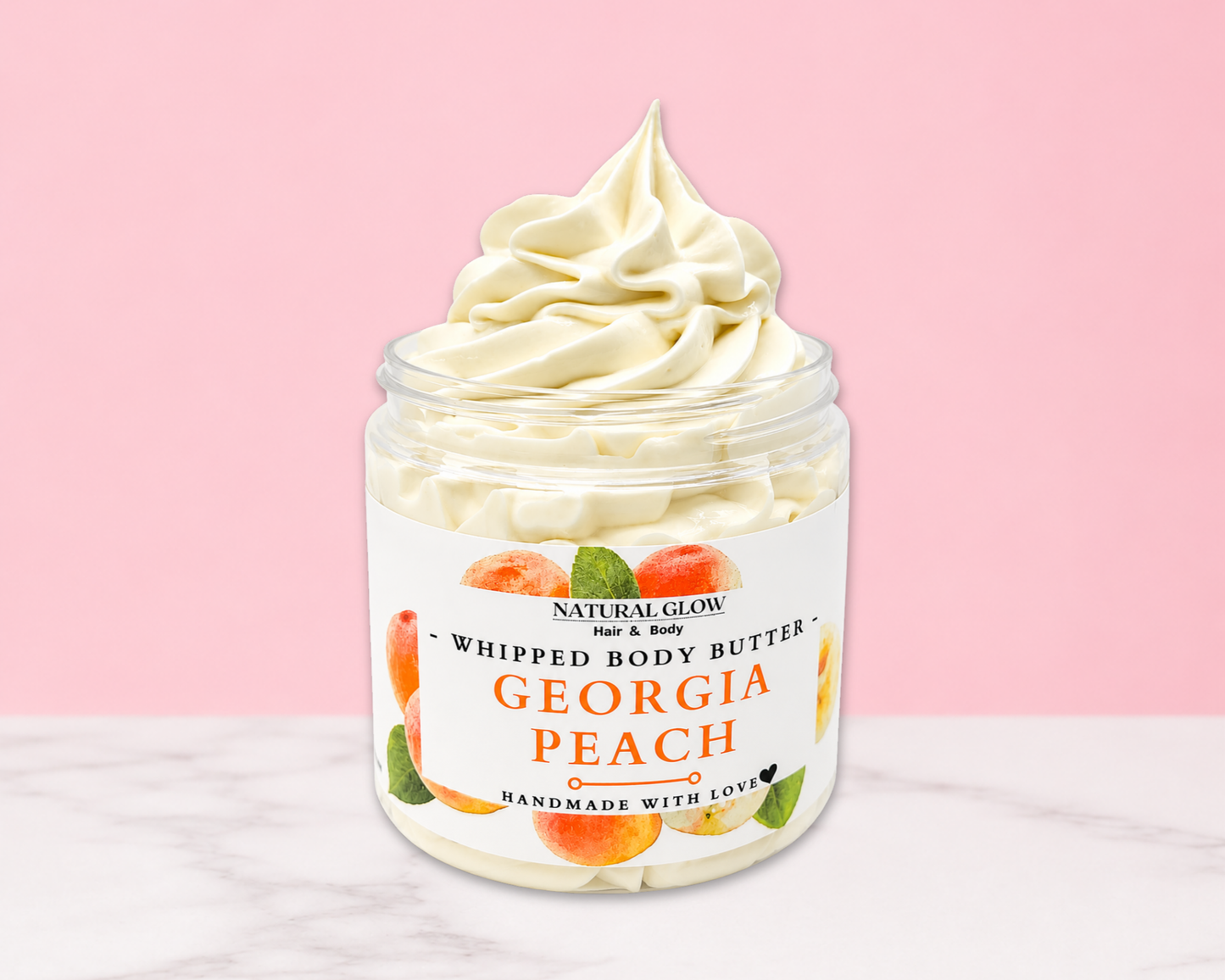 Natural Glow Georgia Peach whipped body butter in a jar with cream-colored butter swirl, pink background, and white marble surface