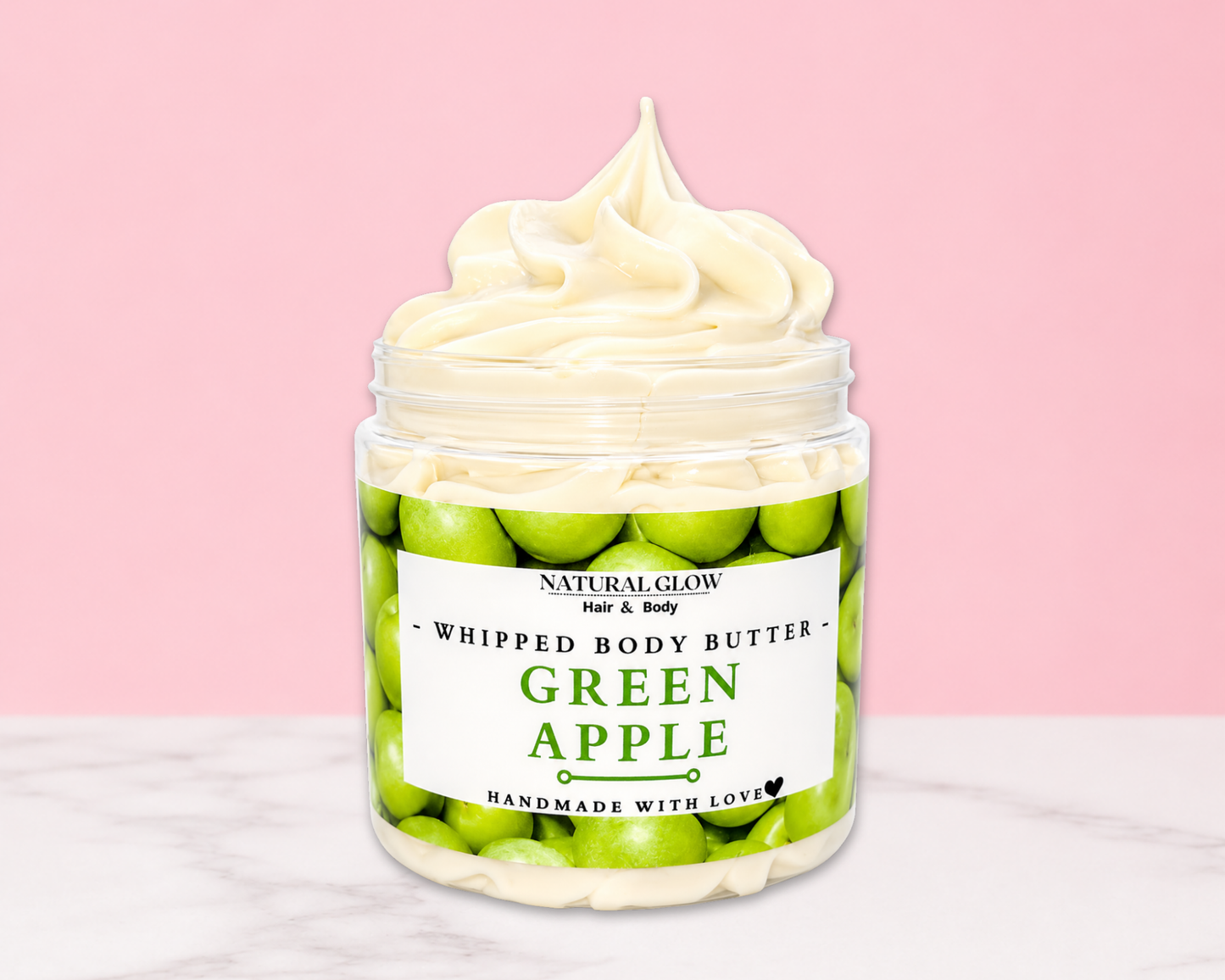 Natural Glow Green Apple whipped body butter in a jar with cream-colored butter swirl, pink background, and white marble surface