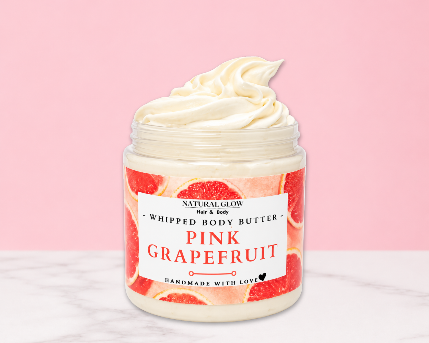 Natural Glow Pink Grapefruit whipped body butter in a jar with cream-colored butter swirl, pink background, and white marble surface