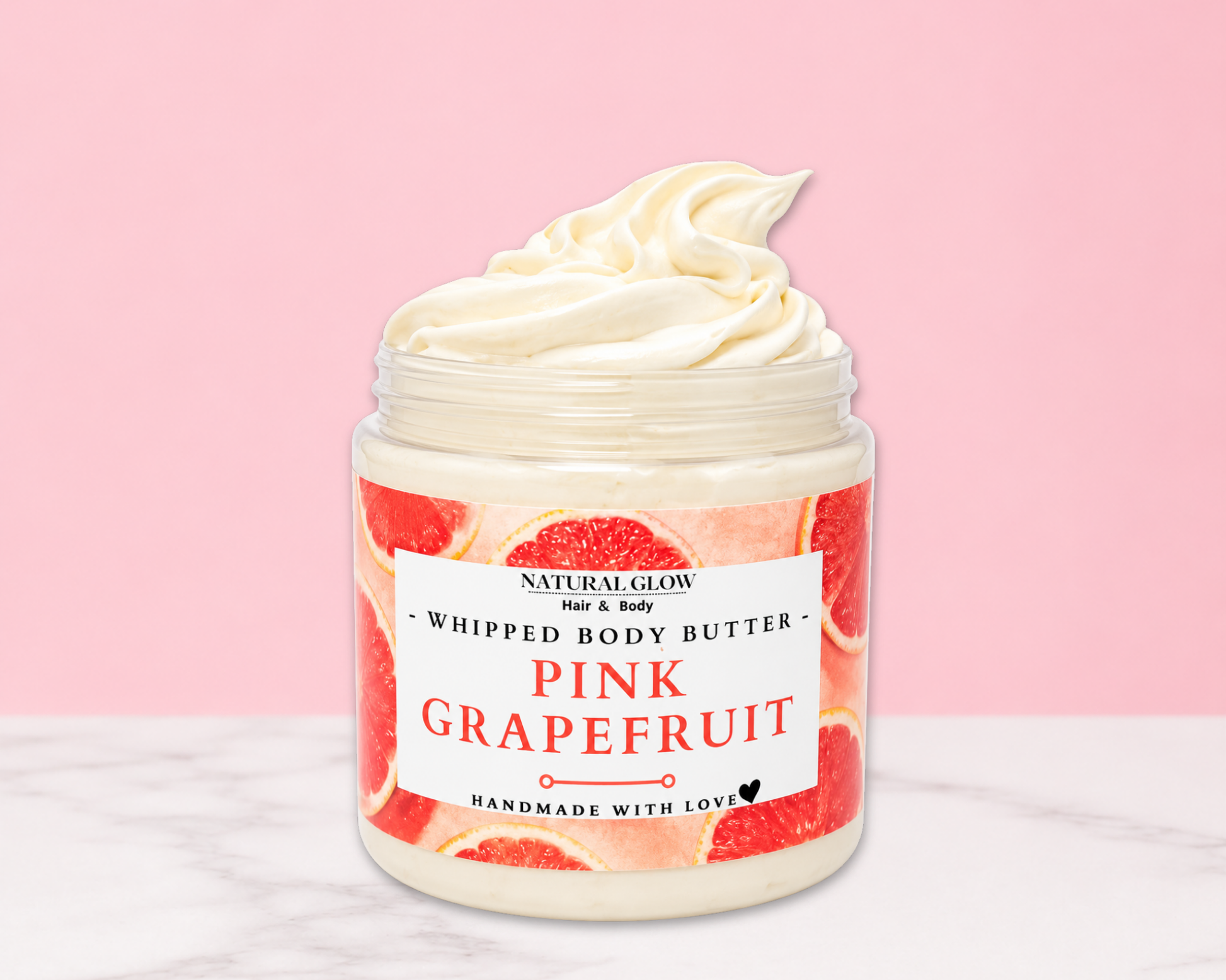 Natural Glow Pink Grapefruit whipped body butter in a jar with cream-colored butter swirl, pink background, and white marble surface