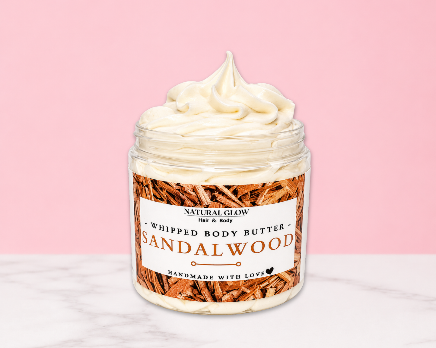 Natural Glow Sandalwood whipped body butter in a jar with cream-colored butter swirl, pink background, and white marble surface