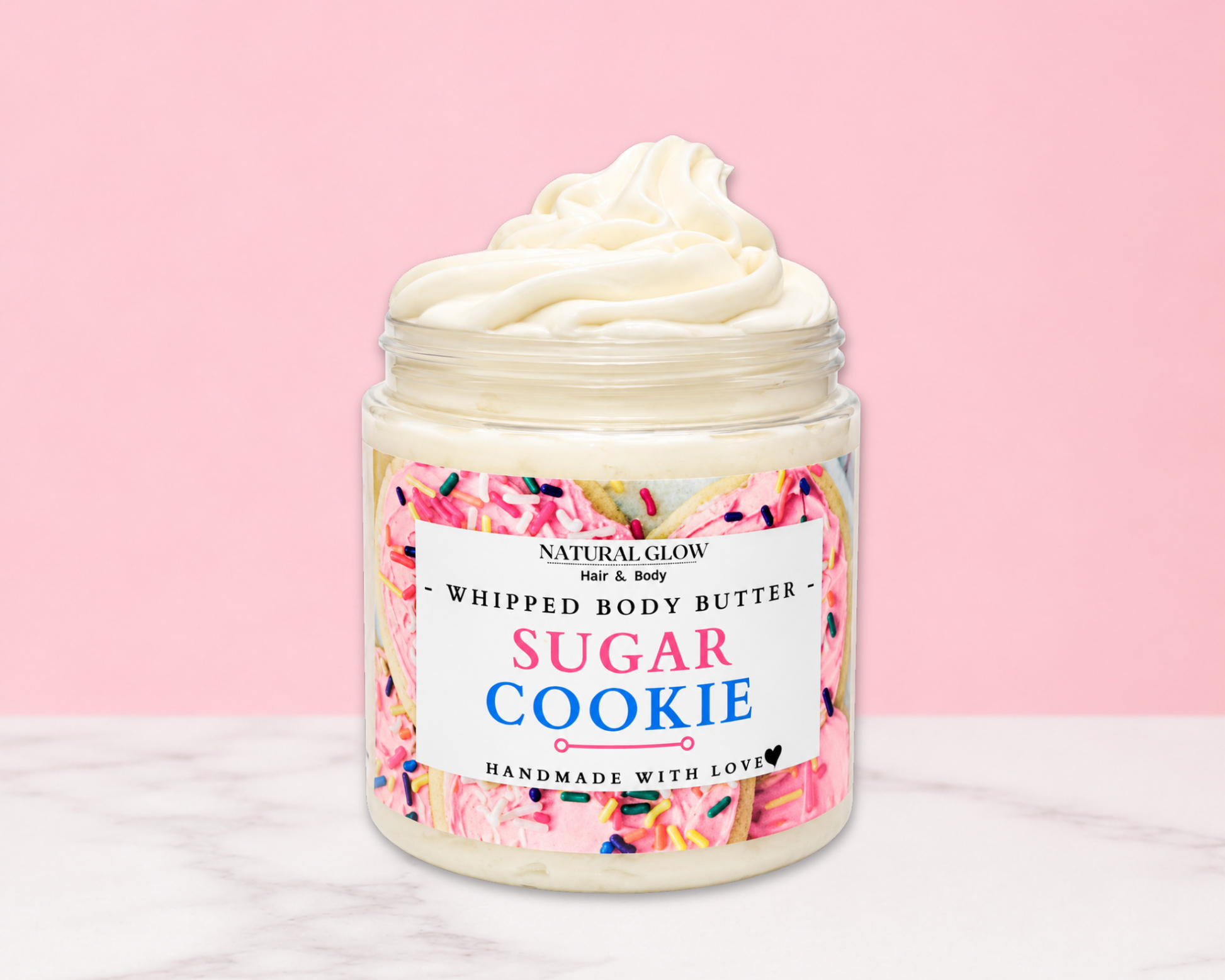 Natural Glow Sugar Cookie whipped body butter in a jar with cream-colored butter swirl, pink background, and white marble surface