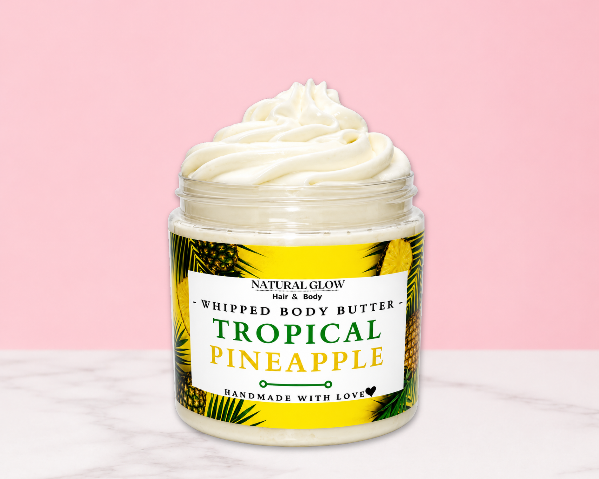 Natural Glow Tropical Pineapple whipped body butter in a jar with cream-colored butter swirl, pink background, and white marble surface