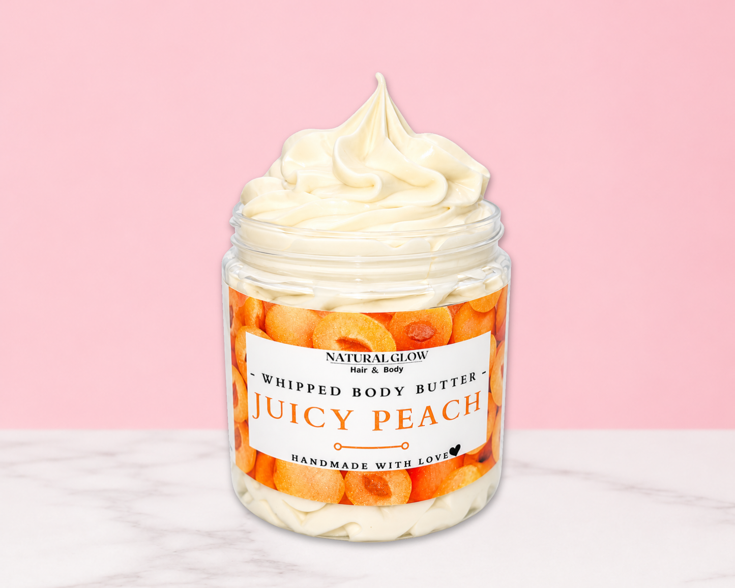 Natural Glow Juicy Peach whipped body butter in a jar with cream-colored butter swirl, pink background, and white marble surface