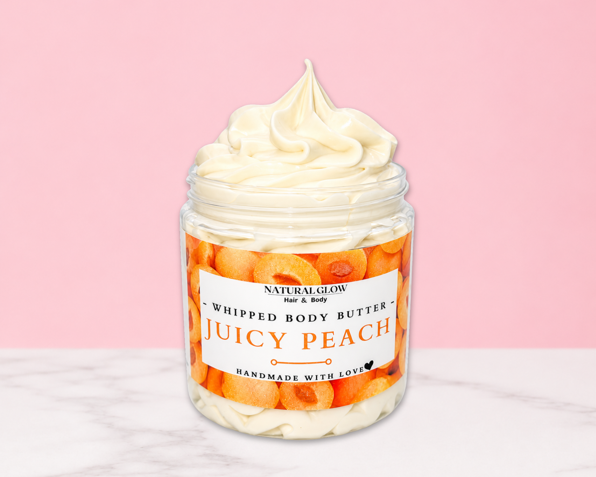 Natural Glow Juicy Peach whipped body butter in a jar with cream-colored butter swirl, pink background, and white marble surface