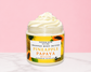 Natural Glow Pineapple Papaya whipped body butter in a jar with cream-colored butter swirl, pink background, and white marble surface