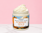 Natural Glow Pumpkin Spice whipped body butter in a jar with cream-colored butter swirl, pink background, and white marble surface